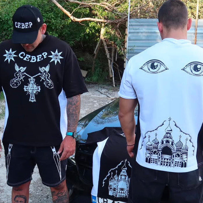 Two men wearing t-shirts with unique designs, one black and one white, standing outdoors.